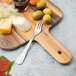 A Walco Marcie stainless steel cocktail fork on a wooden board with cheese and olives.