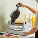 A single Belgian waffle iron with a round waffle inside, being operated on a kitchen counter.
