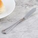 A Walco Marcie stainless steel butter spreader on a table with bread and butter.