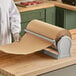 A person in a white coat using a Bulman Deluxe paper cutter to cut brown paper on a counter.