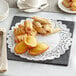 A white plate with a black border and Normandy Lace doilies on a table with pastries and coffee.