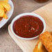 A plate of food on a wooden surface with a white Thunder Group coupe sauce dish filled with red sauce.