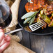 A hand holding a Walco Barony stainless steel table fork over a plate of food.