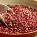 A metal bowl of Amish Country red butterfly popcorn kernels with a scoop.