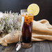 A glass of iced tea with a lemon slice and a Walco stainless steel iced tea spoon on a wooden table.