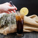 A hand using a Walco Marcie iced tea spoon to stir a glass of iced tea with a lemon slice.