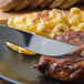 A Walco Barony table knife cutting steak with macaroni and cheese on a plate.