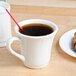 A Tuxton eggshell embossed tall cup of coffee with a plate of croissants on a table.