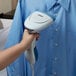 A person using a Conair white handheld steamer to steam a blue shirt.