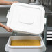 A person holding a white Continental Huskee trash can lid with food in it.
