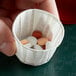 A hand holding a Genpak paper souffle cup with pills in it.