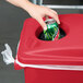 A hand putting a can into a Rubbermaid Slim Jim red trash can.