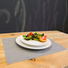 A plate of salad with fruit on a H. Risch, Inc. gray woven vinyl rectangle placemat.