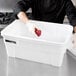 A woman holding an apple in a white Rubbermaid tote with a lid.