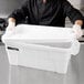 A man in a chef's uniform holding a white Rubbermaid tote with a lid.