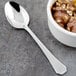 A Walco stainless steel dessert spoon next to a bowl of chocolate ice cream with nuts.