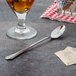 A Walco Prim stainless steel iced tea spoon next to a glass of liquid.