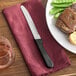 A Libbey stainless steel steak knife on a napkin next to a plate of food.