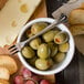 A bowl of green olives and grapes with a Walco stainless steel cocktail fork.