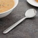 A Walco Maremma bouillon spoon next to a bowl of soup.