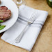 A Walco stainless steel dinner fork on a napkin next to a plate of food.