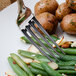 A Walco stainless steel dinner fork on a plate of green beans and potatoes.