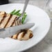 A Libbey steak knife cutting a piece of chicken on a plate with green beans and a knife and fork.