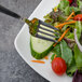 A Walco stainless steel salad fork on a plate of salad with cucumber and tomatoes.