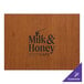 A rectangular wooden placemat with the Milk & Honey Cafe logo on it.