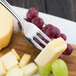 A Walco Prim stainless steel cocktail fork holding cheese and grapes.