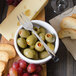 A Walco Freya cocktail fork in a bowl of green olives and red grapes.