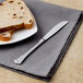 A Walco stainless steel butter knife on a table with a plate of bread.