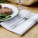 A Walco stainless steel table fork on a napkin next to a plate of food.