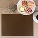 A brown rectangular vinyl placemat on a table with a plate of pastries and a cup of coffee.