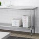 A Regency stainless steel work table undershelf with plastic containers on it.