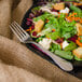 A Walco stainless steel salad fork on a plate of salad with vegetables and cheese.