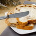 A Walco stainless steel butter knife spreading butter on a piece of bread.
