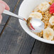 A Walco Prim stainless steel teaspoon in a bowl of oatmeal with bananas and strawberries.