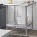 A metal Regency work table with an undershelf holding a white plastic container with blue writing.