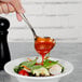 A Walco stainless steel gravy ladle pouring red sauce over a salad