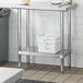 A metal shelf holding a white plastic container on a Regency stainless steel work table.