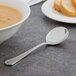 A bowl of soup with a Walco Prim bouillon spoon on a table with bread.