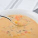 A Walco stainless steel bouillon spoon holding soup with vegetables and rice.
