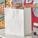 A woman holding a Duro white paper shopping bag full of bread.