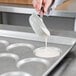A person pouring white liquid into a Chicago Metallic ePAN of muffins.