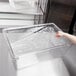 A hand placing a clear plastic drain tray in a clear plastic food box.