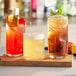 A wooden tray with 3 Acopa Thumbprint beverage glasses filled with beer, ice tea, and a third drink.