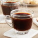 Two Acopa glass coffee cups filled with coffee on a table.