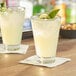 Two Acopa Fusion beverage glasses filled with lemonade and garnished with cucumber and mint on a table.