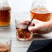 A hand holding an Arcoroc Broadway Rocks glass with brown liquid.